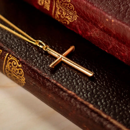 gold cross necklace with chain placed on a book